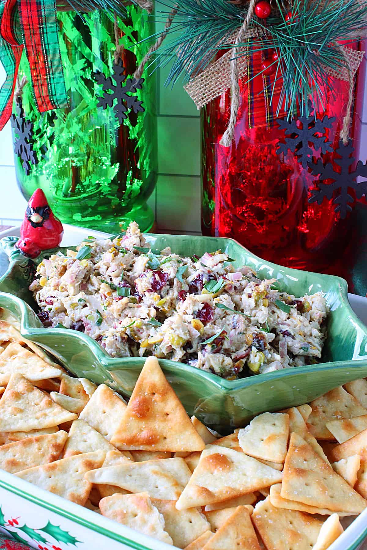 Two red and green hurricane lanterns in front of a bowl of Christmas Chicken Salad.