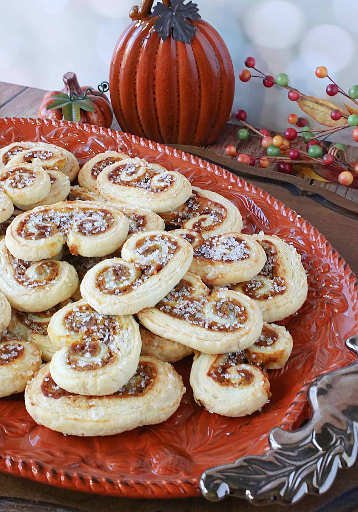 Two ceramic pumpkins along with an orange ceramic platter filled with Pumpkin Spice Palmiers.