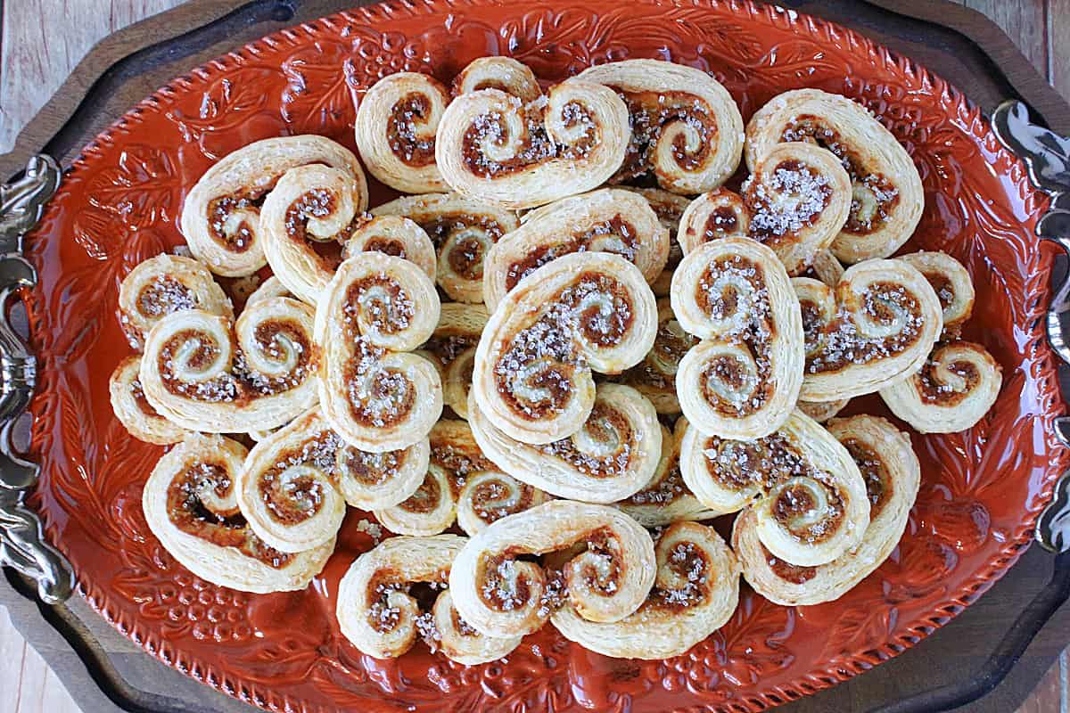 An overhead photo of a orange oval platter filled with Pumpkin Spice Palmiers topped with sanding sugar.