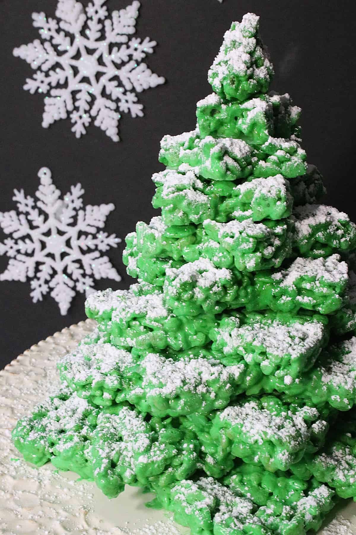 A 3D Rice Krispies Treats Christmas Tree with a black background and snowflakes.