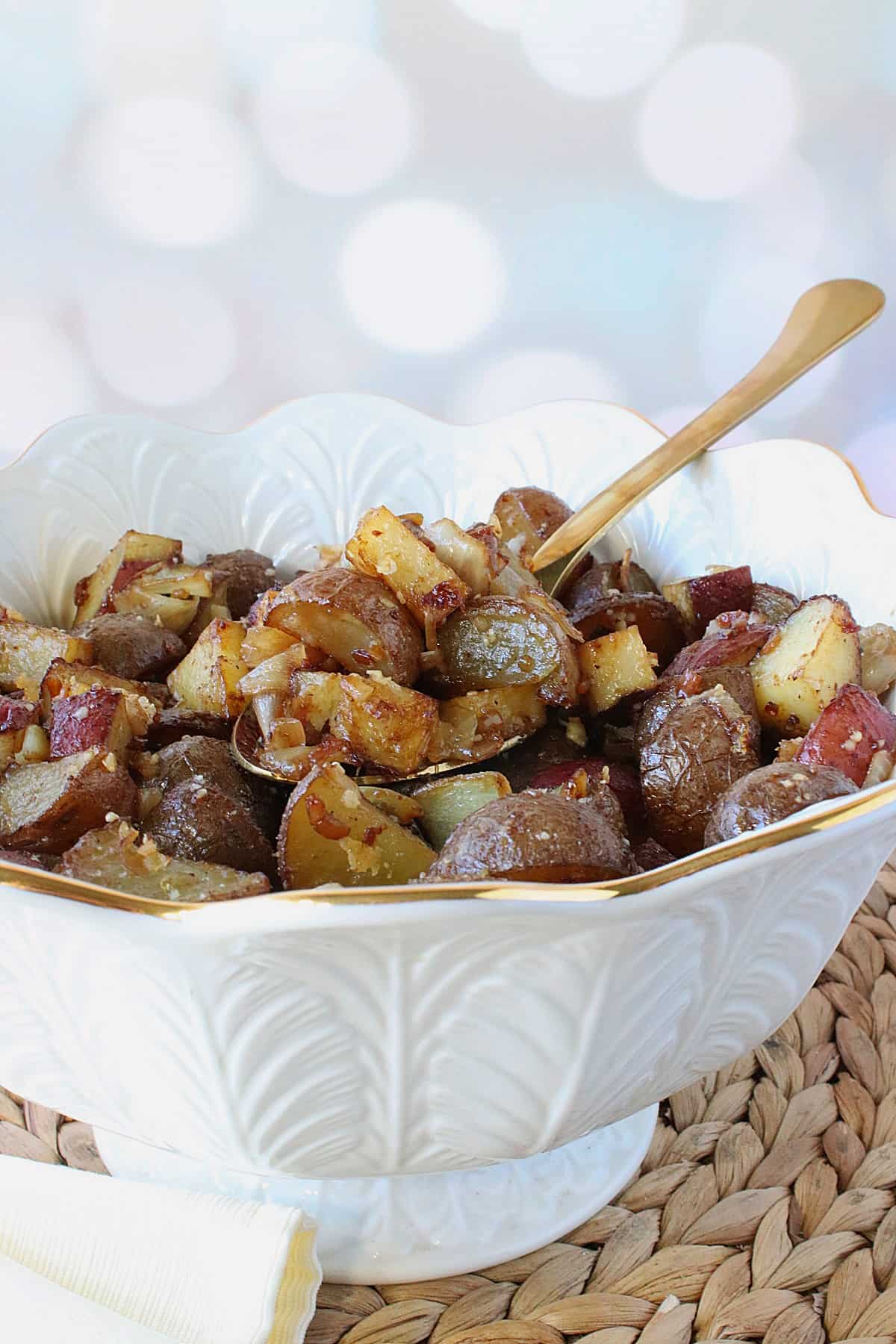 A pretty white bowl filled with Roasted Potatoes with Onions and Parmesan along with a spoon.