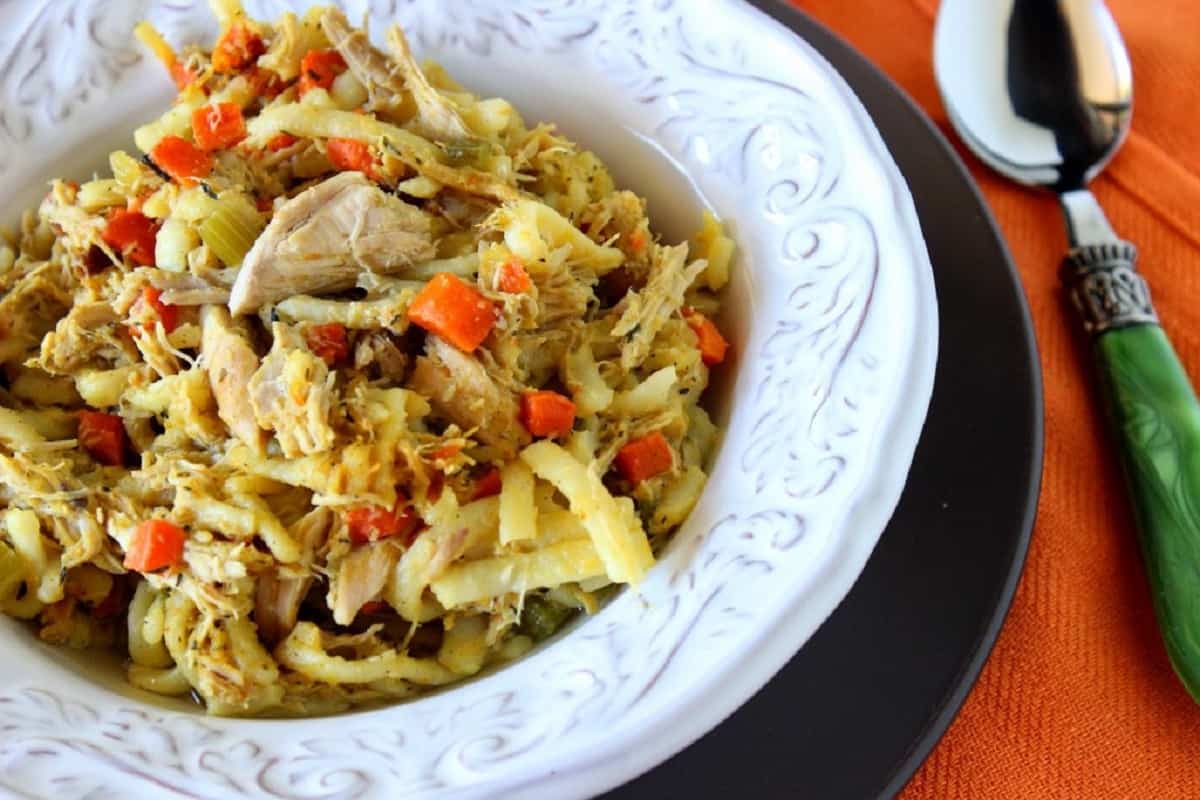 A white bowl filled with Carrot Ginger Chicken Noodle Stew and a spoon.