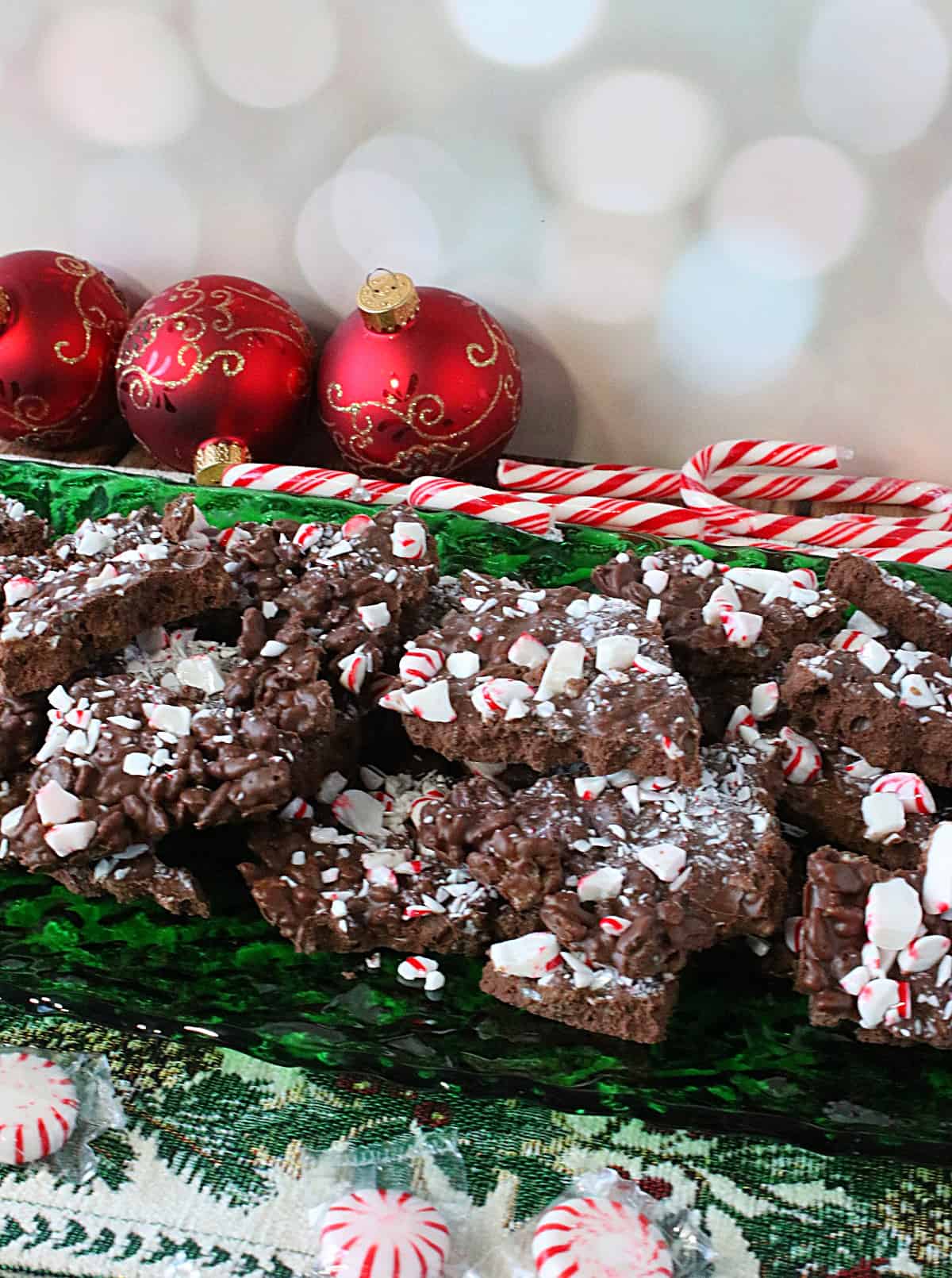 A green glass plate filled with Cocoa Krispies Peppermint Bark with candy canes in the background.