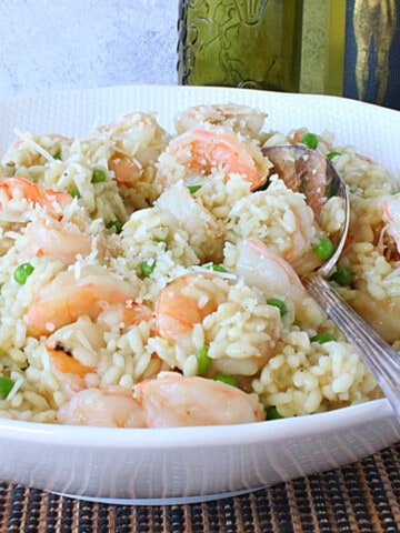 A delicious looking Shrimp Scampi Risotto with Wine and Parmesan in a white bowl with a serving spoon.