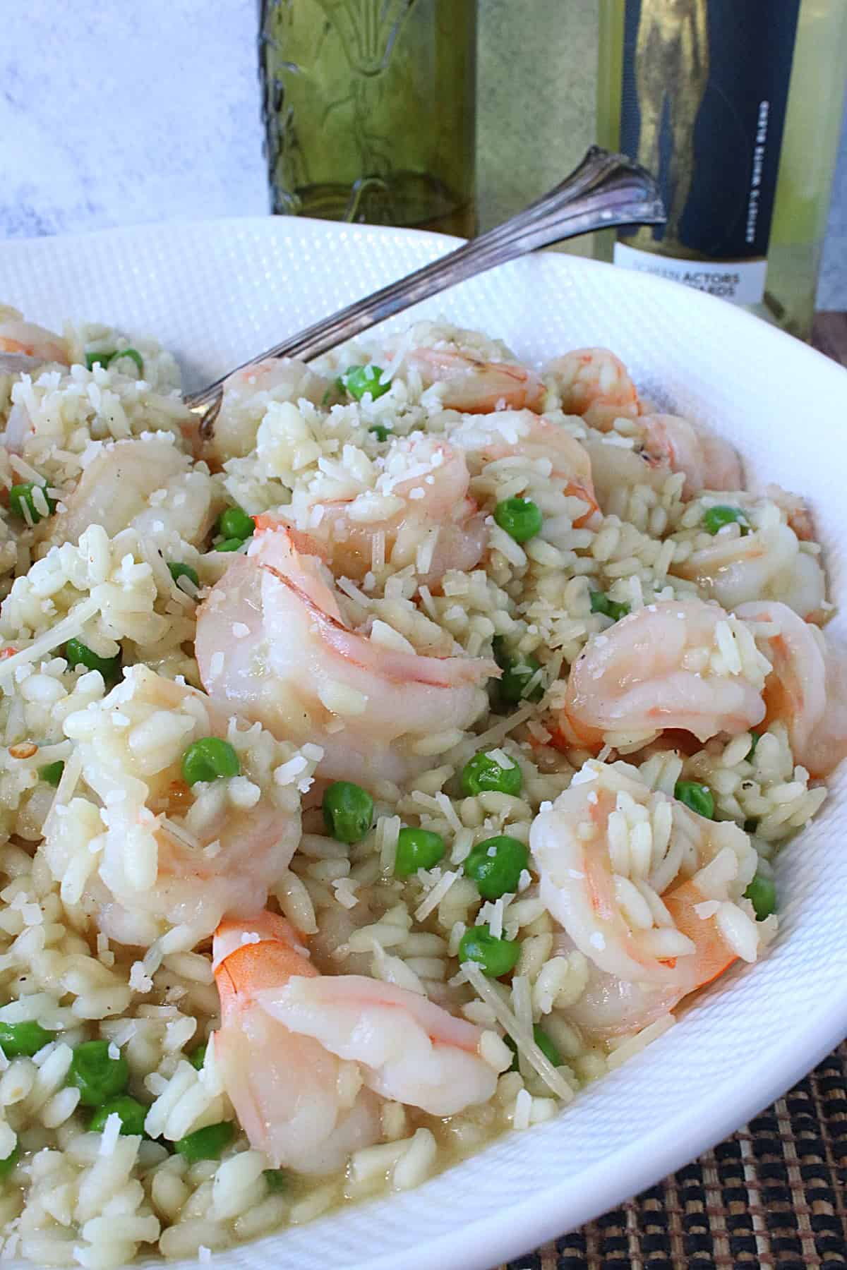 Shrimp scampi risotto with pink shrimp and peas in a white bowl with a spoon.