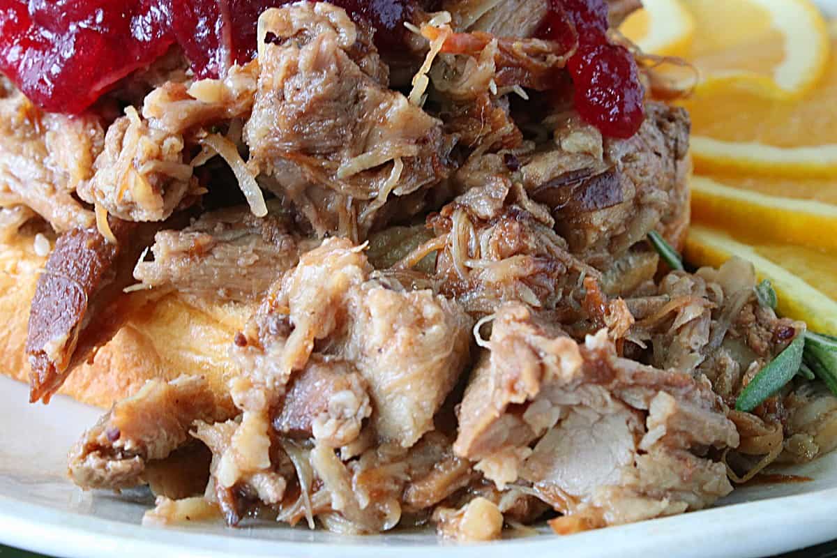 A closeup of Cranberry Pulled Pork with cranberry sauce and orange slices in the background.