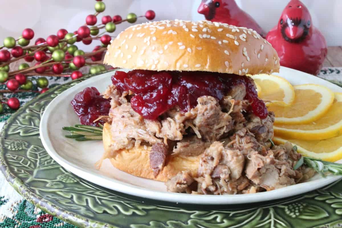 A delicious Cranberry Pulled Pork sandwich on a green plate with orange slices.