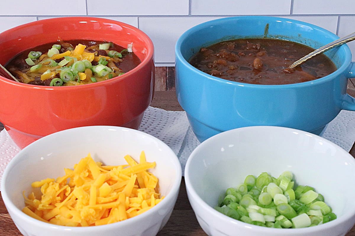 Two bowls of Baked Bean Soup with Beef and Bacon and two bowl of toppings in the foreground.