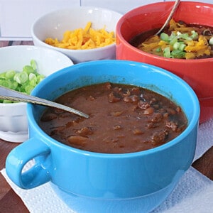A blue bowl filled with Baked Bean Soup with Beef and Bacon along with a spoon.