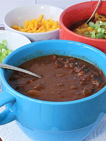 A blue bowl filled with Baked Bean Soup with Beef and Bacon along with a spoon.