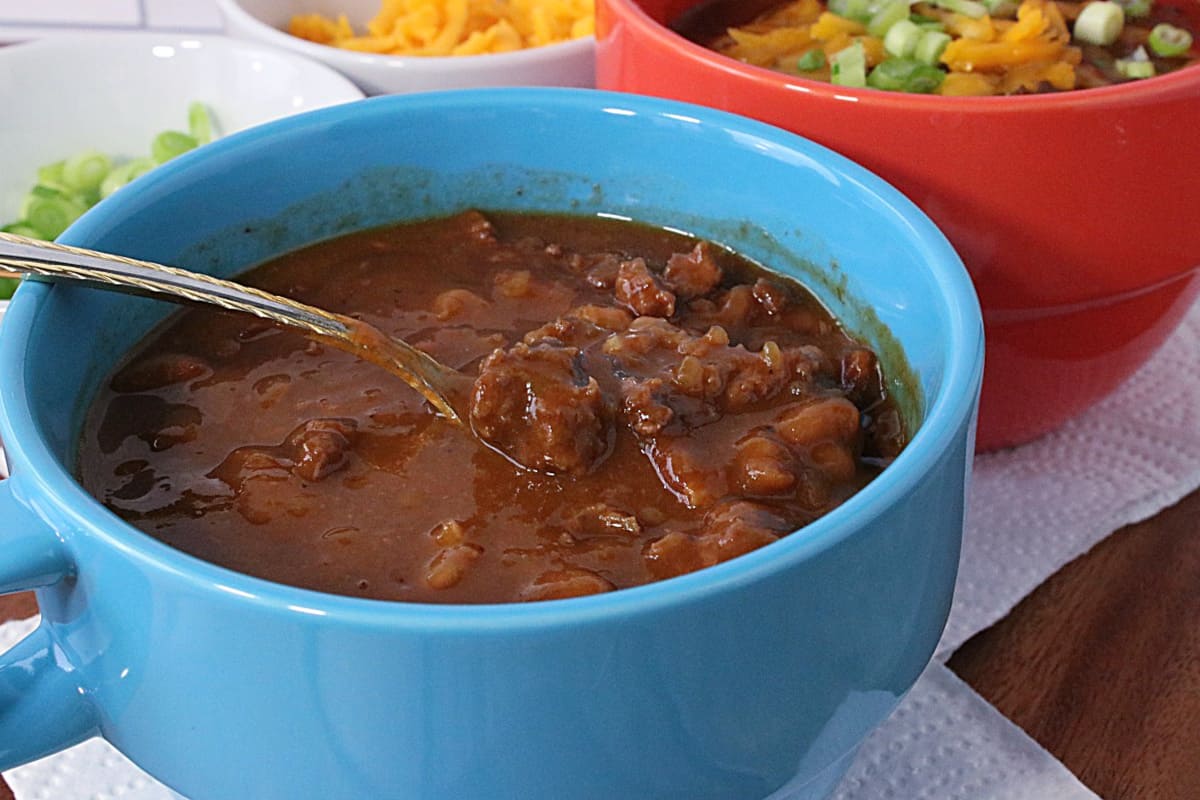 A delicious looking blue bowl of Baked Bean Soup with Beef and Bacon with a spoon.