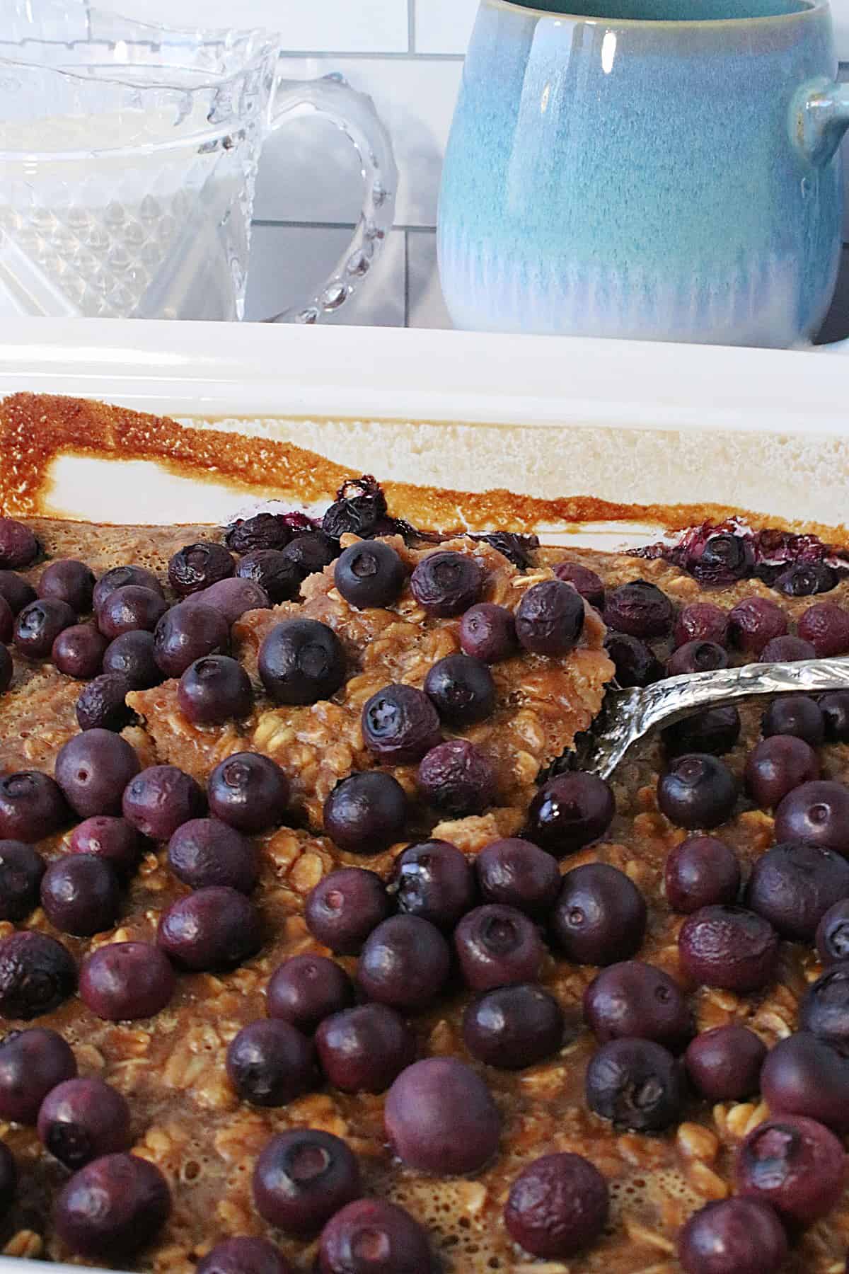 A serving spoon scooping out a portion of Baked Peanut Butter and Jelly Oatmeal in a casserole dish.