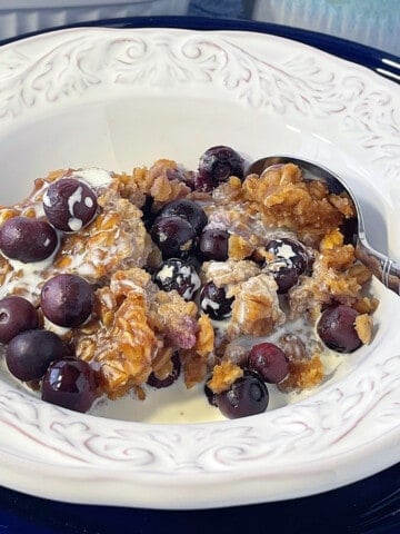 A white bowl filled with a serving of baked peanut butter and jelly oatmeal along with a spoon.