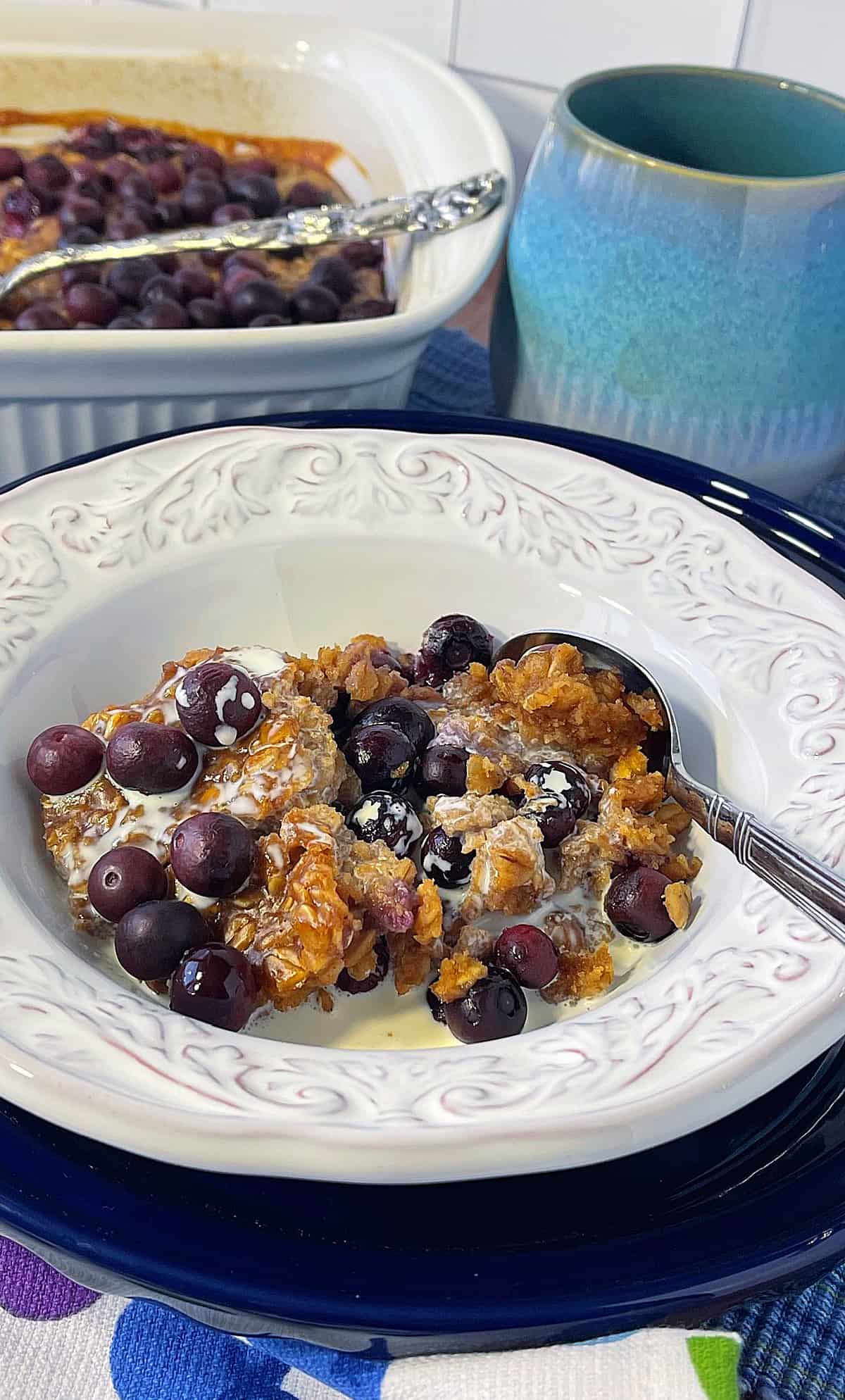 A serving of Baked Peanut Butter and Jelly Oatmeal in a white bowl with a casserole dish in the background.