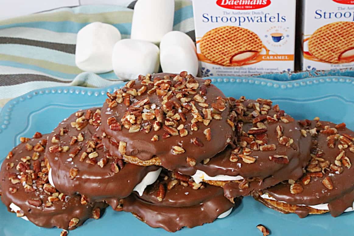 Chocolate covered S'mores Stroopwafel Sandwiches on a blue plate with marshmallows in the background.
