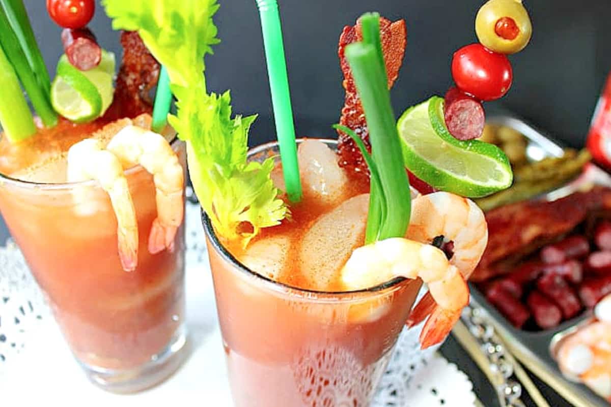 A look inside two glasses filled with Bacon Bloody Mary's with shrimp, scallions, sausage, and olives.