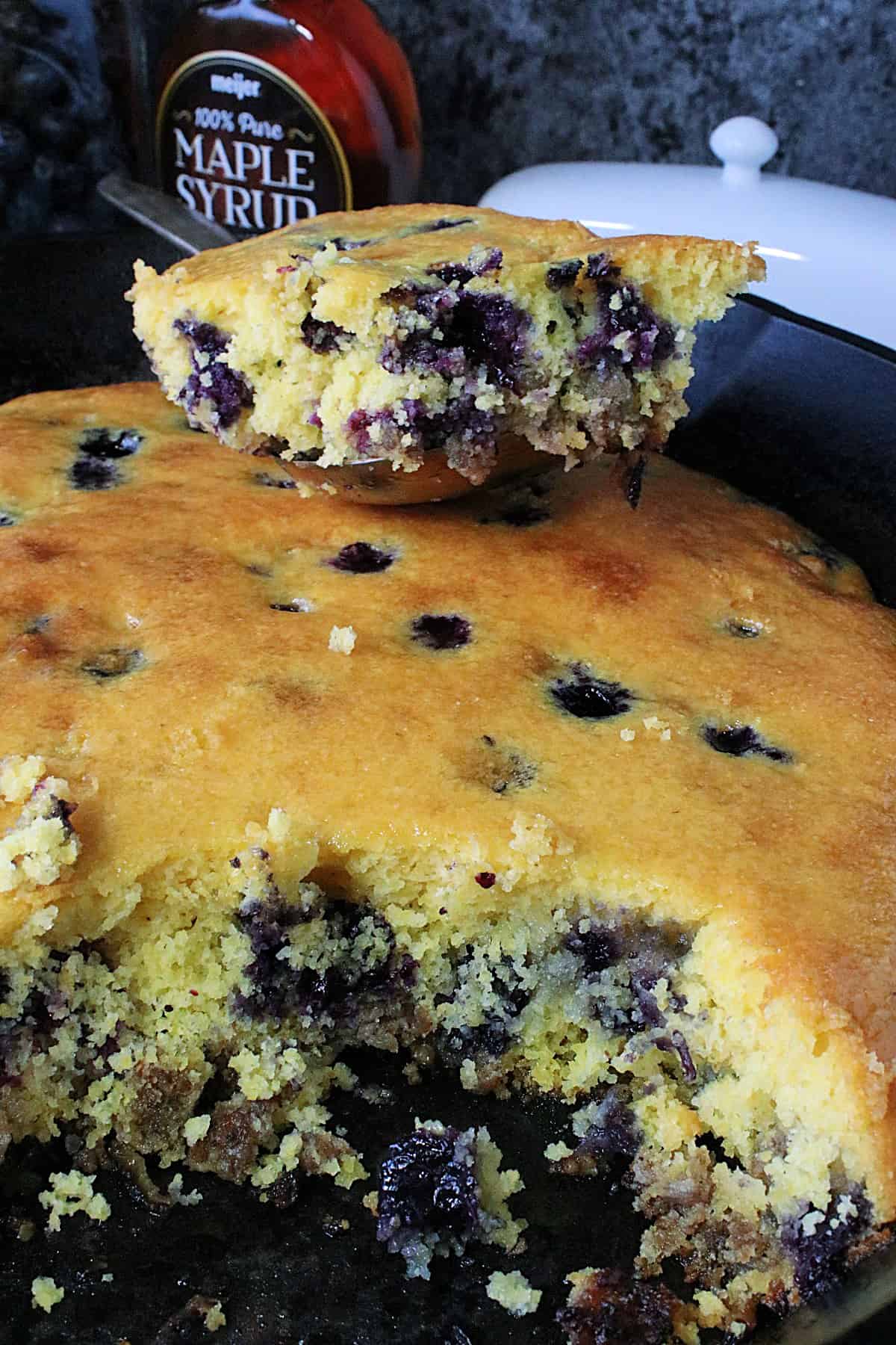 A scoop of Cornbread Breakfast Casserole with blueberries and sausage taken from a cast iron skillet.