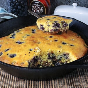 A cast iron skillet with a golden baked Cornbread Breakfast Casserole with Sausage and Blueberries.