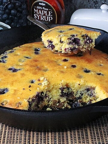 A cast iron skillet with a golden baked Cornbread Breakfast Casserole with Sausage and Blueberries.