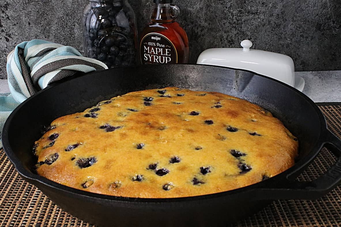 A cast iron skillet with a golden Cornbread Breakfast Casserole with Sausage and Blueberries inside.