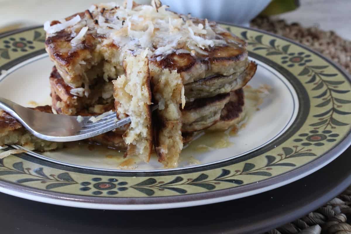 A fork with a bite of oatmeal pancakes with coconut.