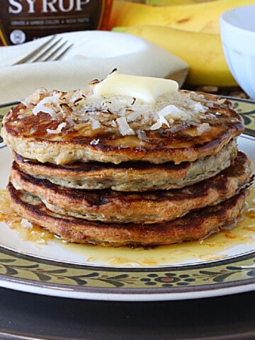 A stack of Oatmeal Pancakes topped with coconut and butter.