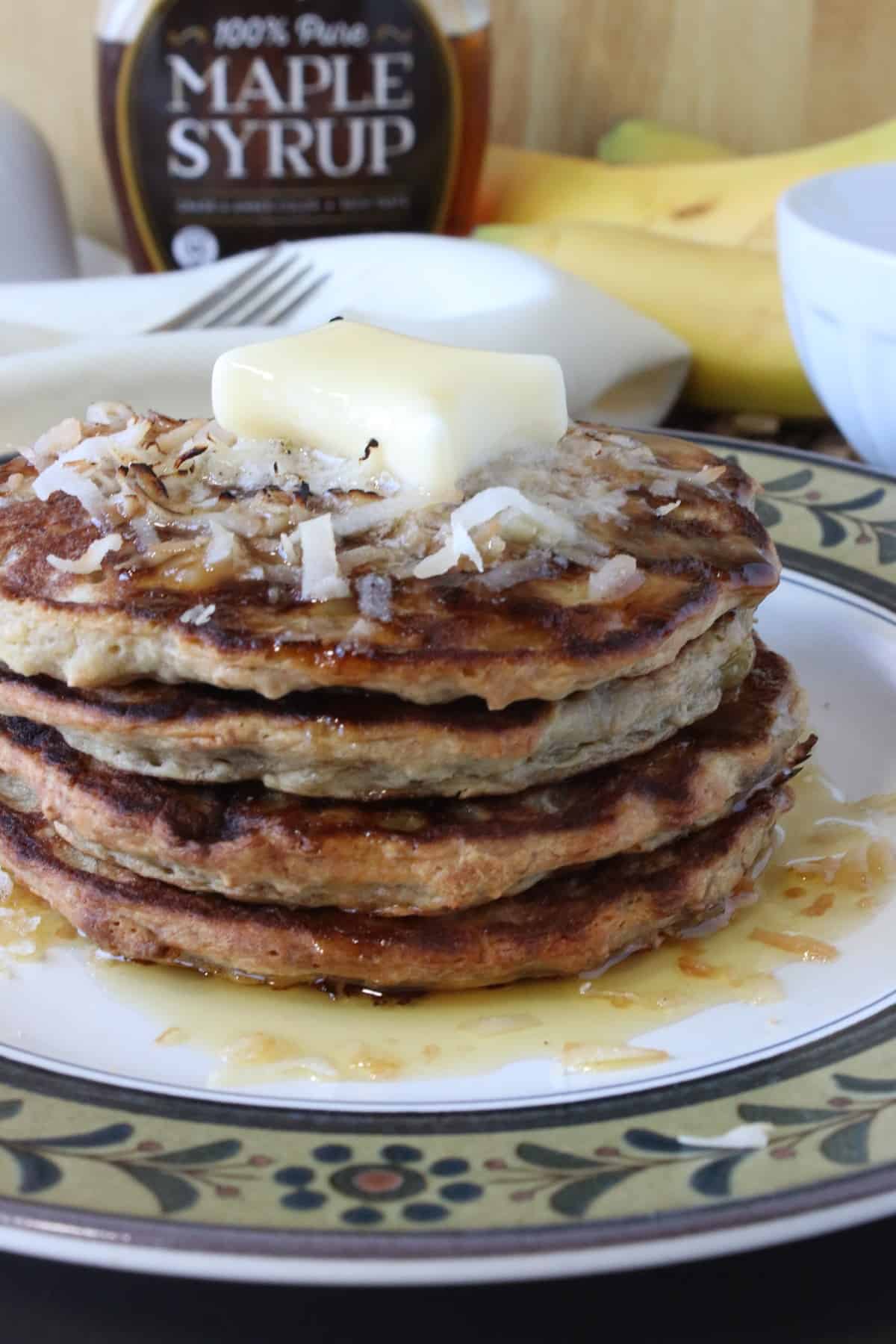 A stack of four Oatmeal Pancakes with Banana and Coconut on a plate with butter.