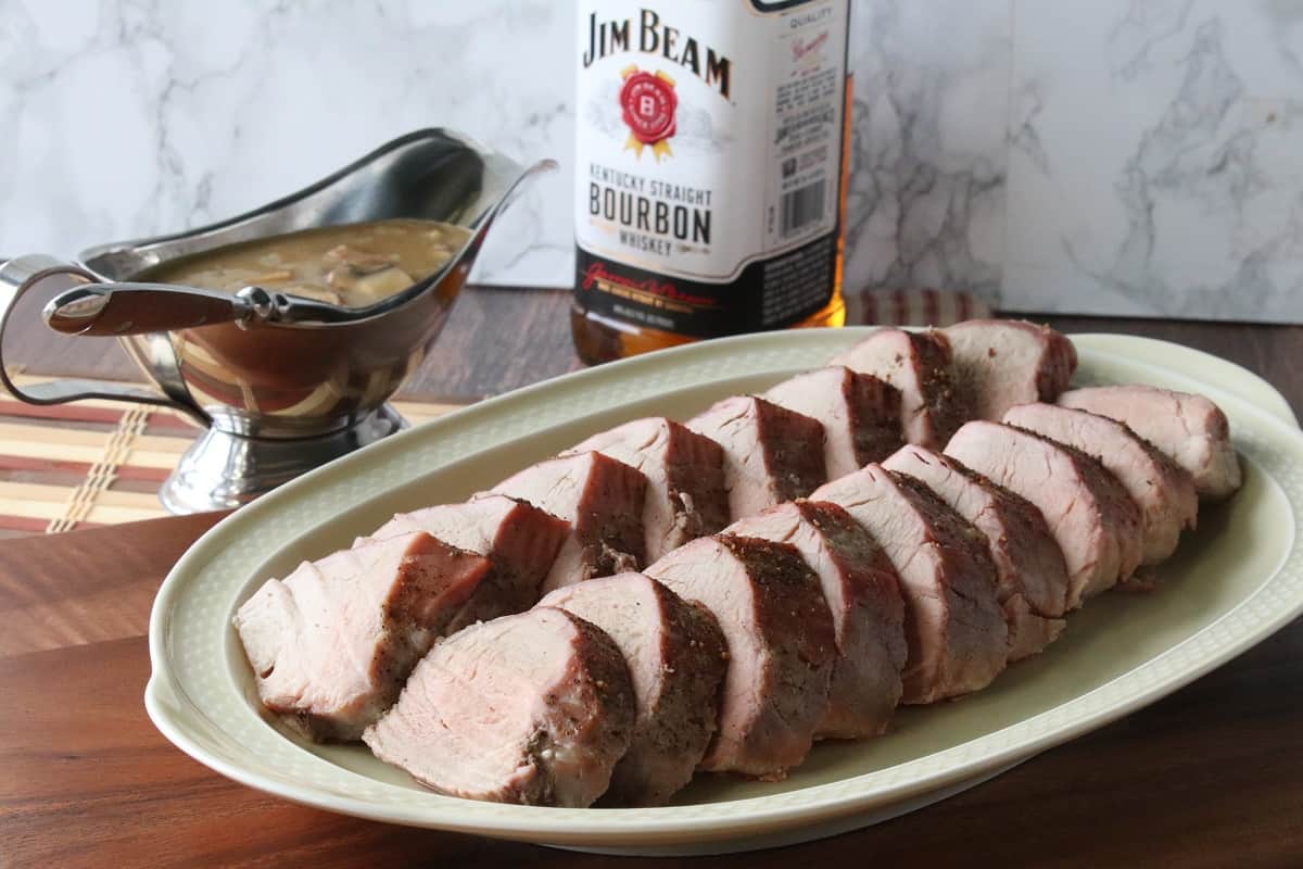 A sliced pork tenderloin on a platter with mushroom bourbon gravy on the side.