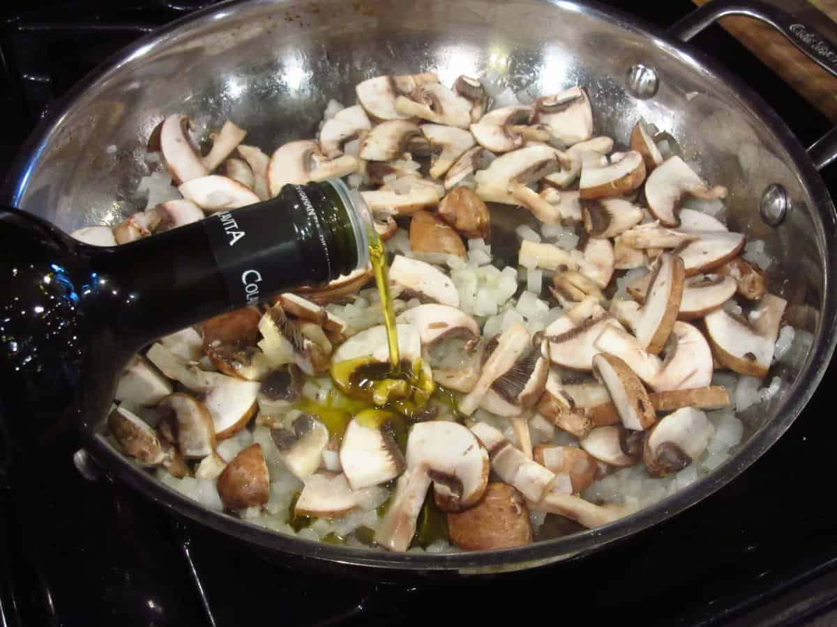 Olive oil being added to mushrooms in a skillet.
