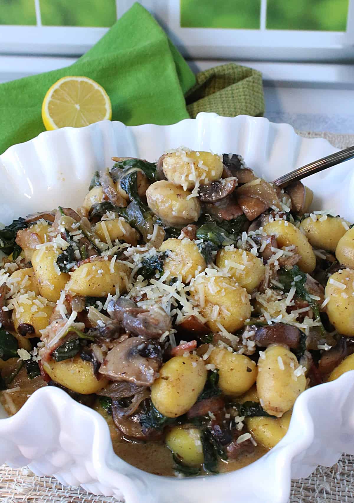 A fluted white bowl filled with Potato Gnocchi with Spinach and Mushrooms.