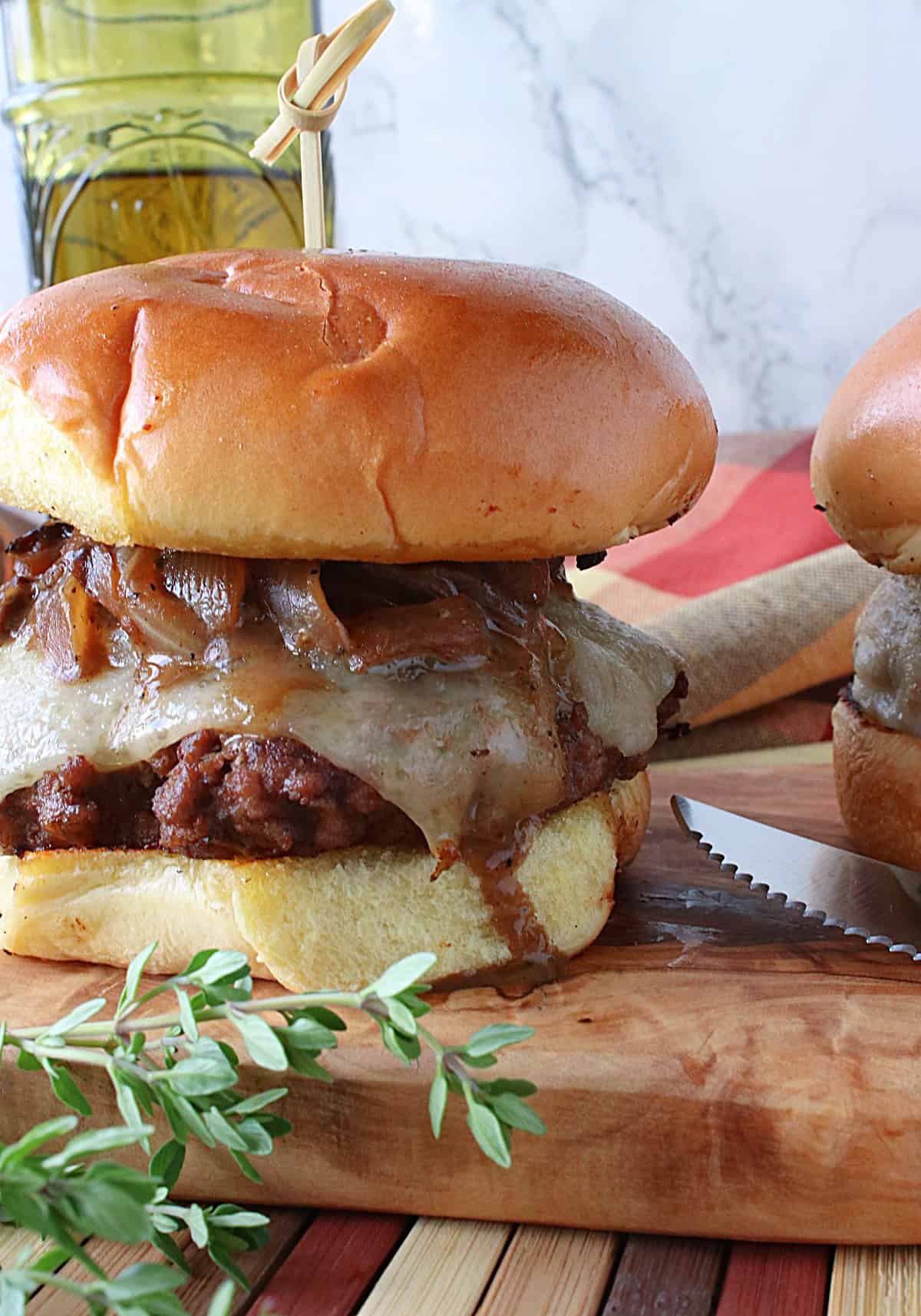 A plump Mushroom Swiss Burger topped with onions and cheese on a wooden board.