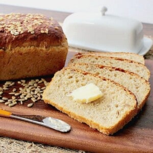 Slices of Oatmeal Honey Bread with Sunflower Seeds on a cutting board along with a pat of butter.