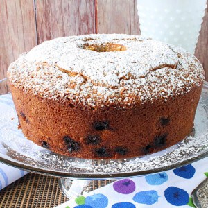 A Sour Cream Poundcake with Blueberry and Orange on a glass cake stand with powdered sugar on top of the cake.