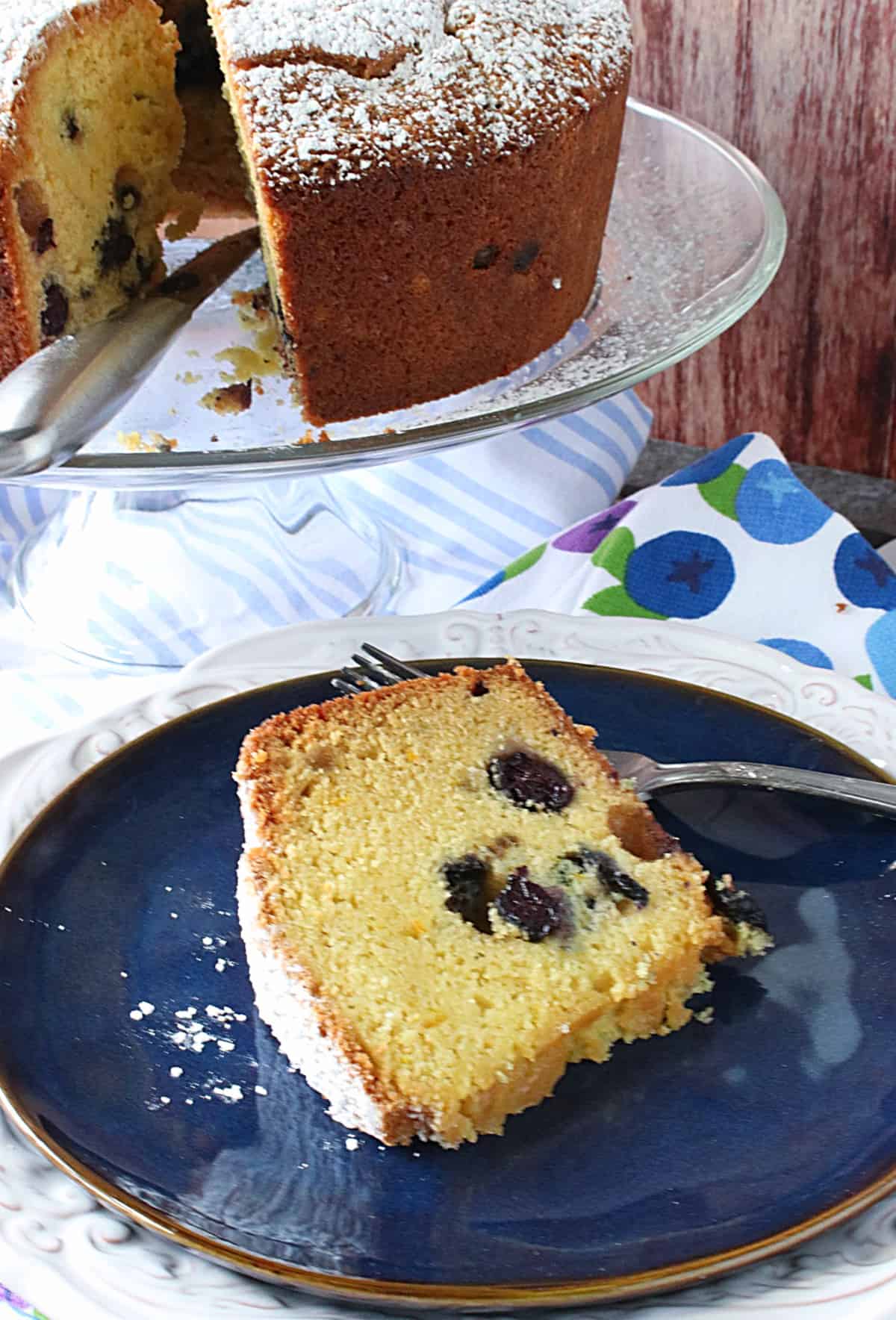 A slice of Sour Cream Poundcake with Blueberries and Orange on a blue plate with a fork.