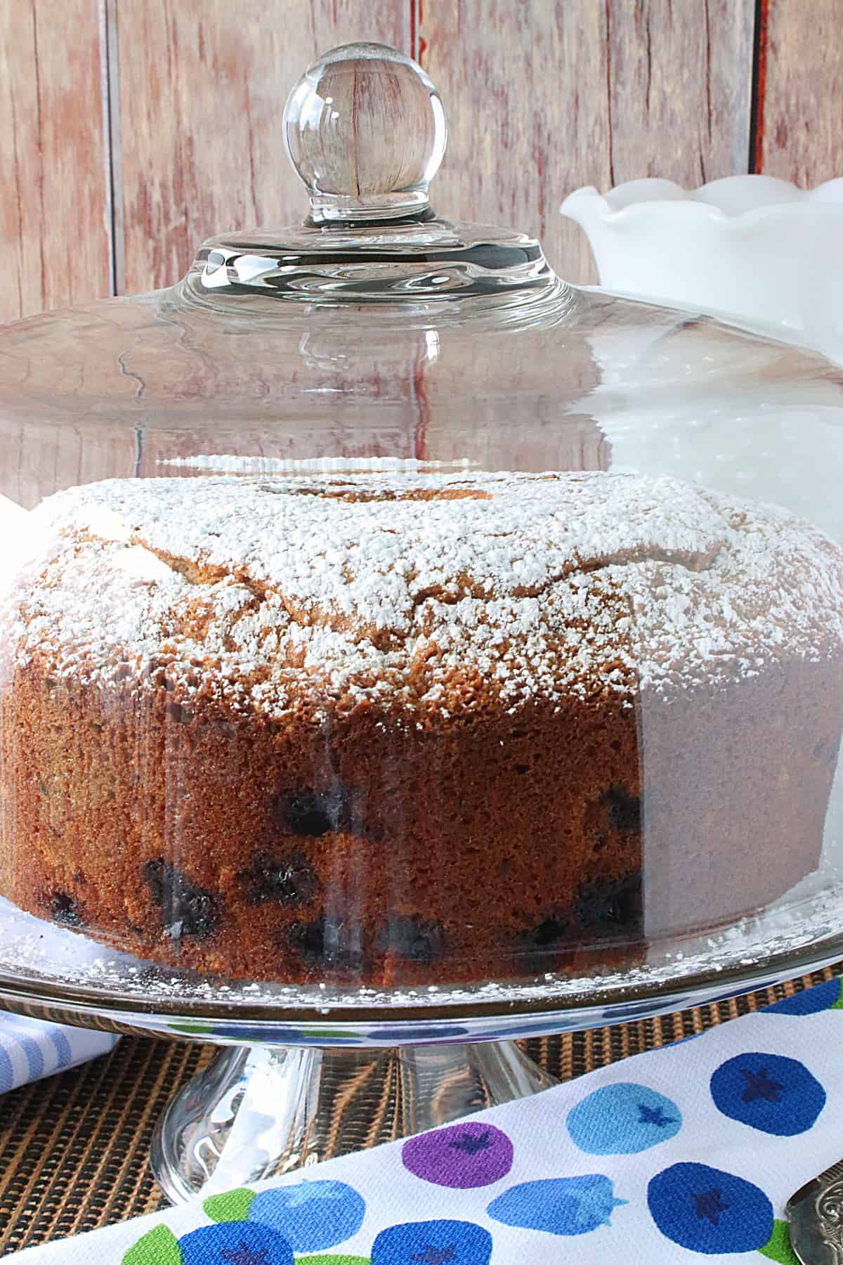 A Sour Cream Poundcake on a glass cake stand with a dome over the top of the cake.