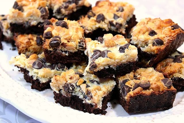 A white plate topped with golden brown Coconut Brownies with chocolate chips and macadamia nuts.