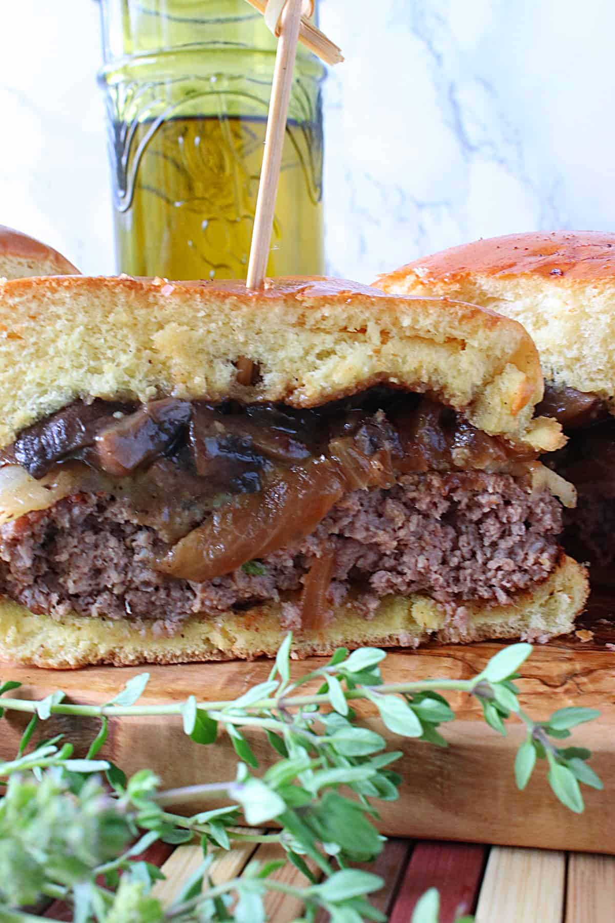 A half a Mushroom Swiss Burger on a wooden board with a toothpick sticking in it.