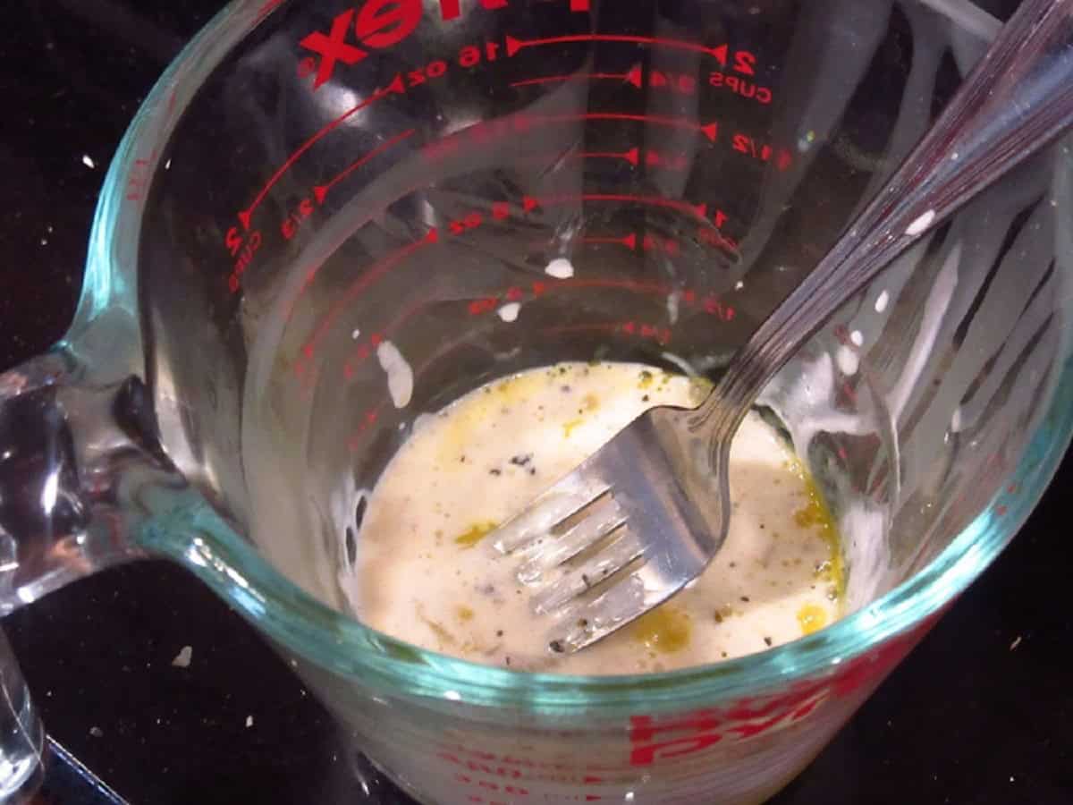 A fork and an egg in a glass measuring cup.