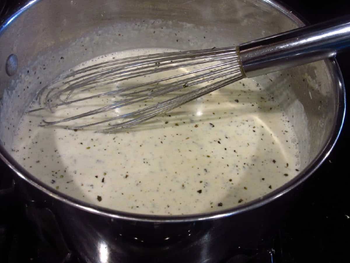 A whisk in a saucepan with homemade Alfredo Sauce.