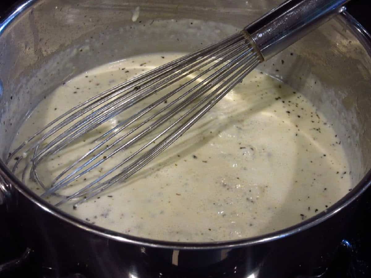 Homemade Alfredo sauce with seasonings in a saucepan with a whisk.