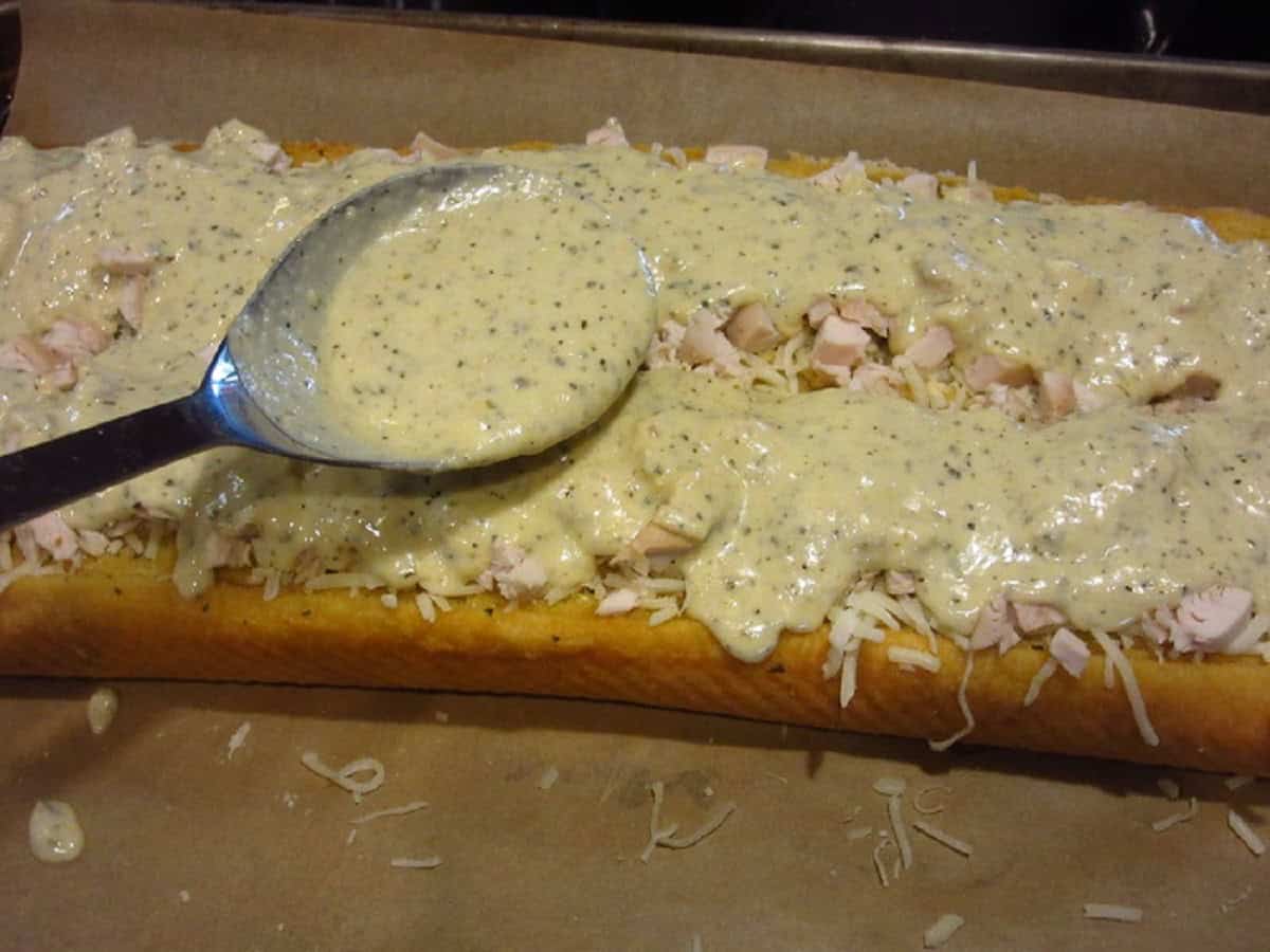 Alfredo sauce being spooned over a Chicken Alfredo Garlic Bread Pizza.