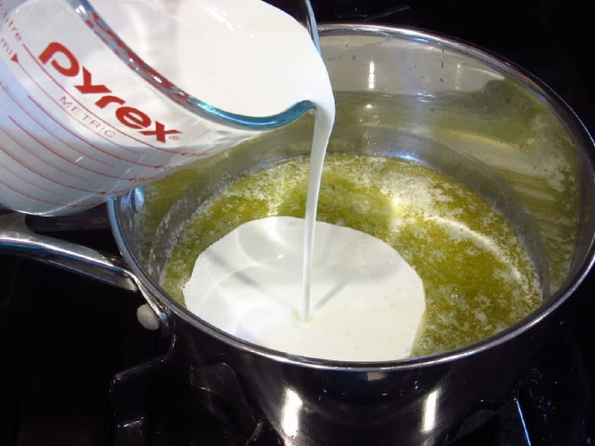 Heavy cream being added to a saucepan to make Alfredo sauce.