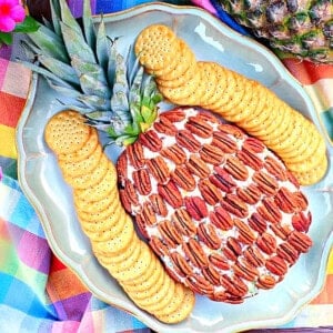 A cute Pineapple Shaped Cheese Ball on a platter surrounded by crackers and a colorful napkin.