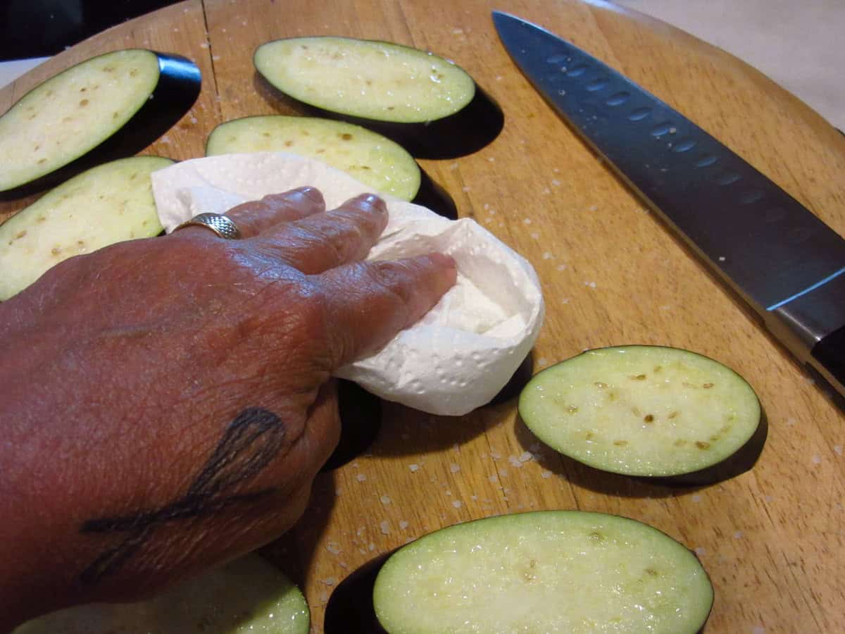 A hand with a paper towel drying off eggplant slices.