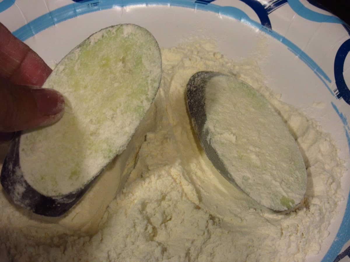 Eggplant slices being dredged in flour.