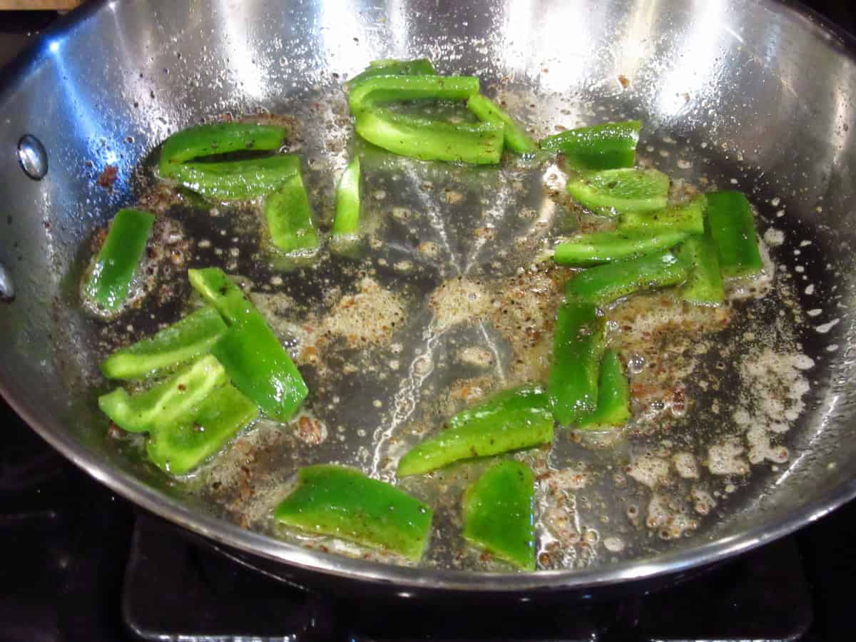 Cooking cut green peppers in a skillet.