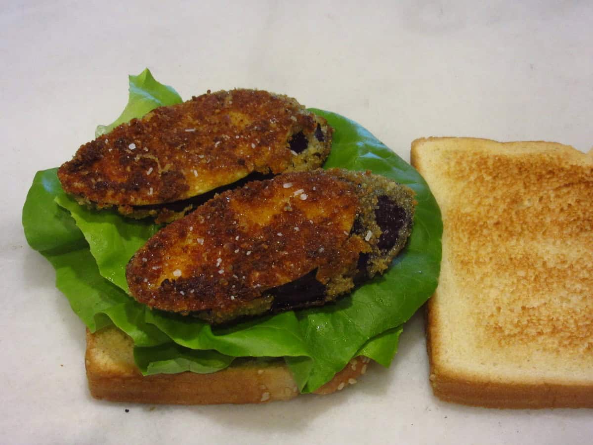Fried eggplant on top of lettuce leaves for a sandwich.