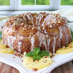 A pretty glazed Hummingbird Upside Down Bundt Cake on a platter with mint and pecans.