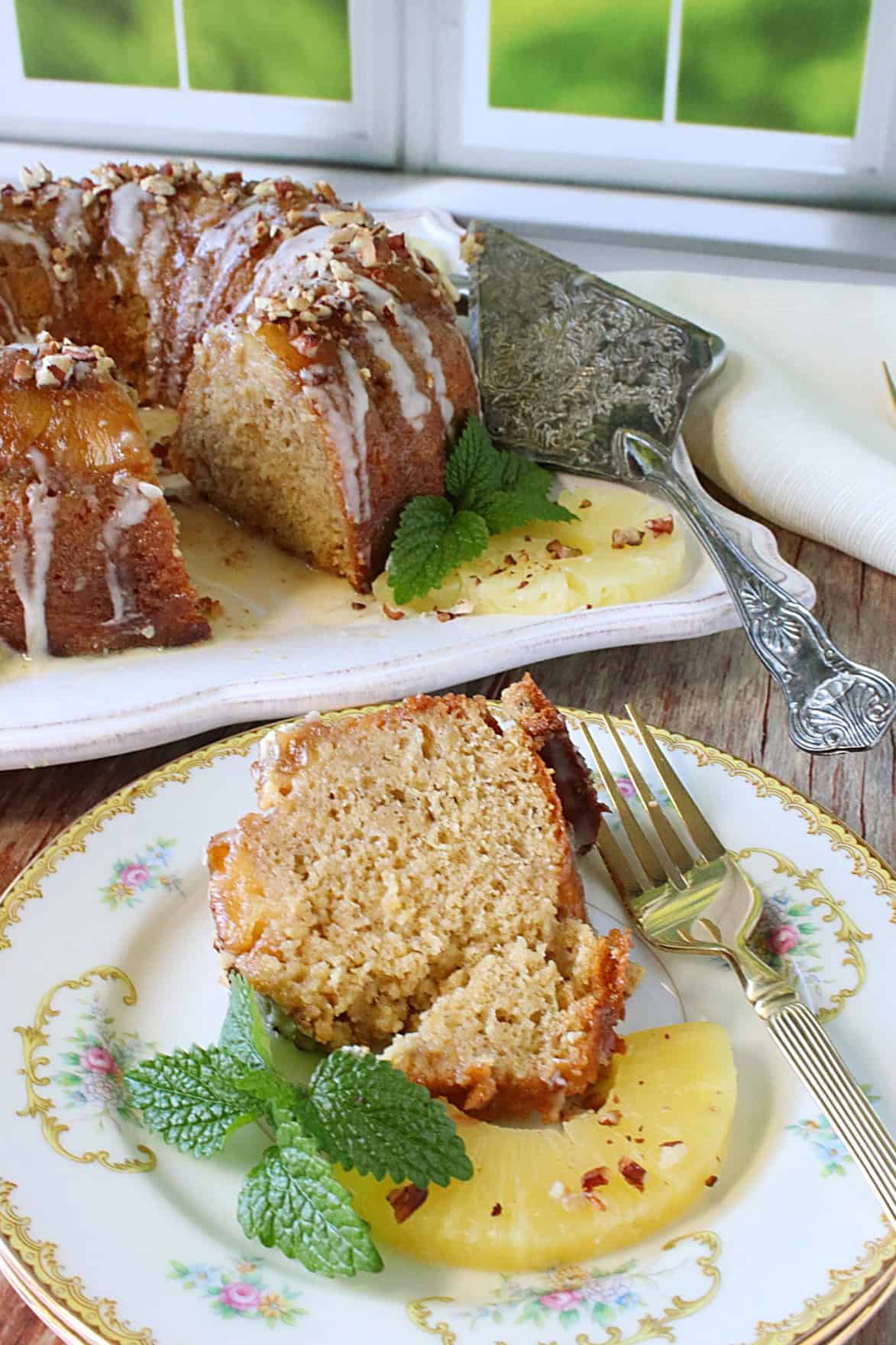 A slice of hummingbird cake in the foreground with a whole cake in the background.