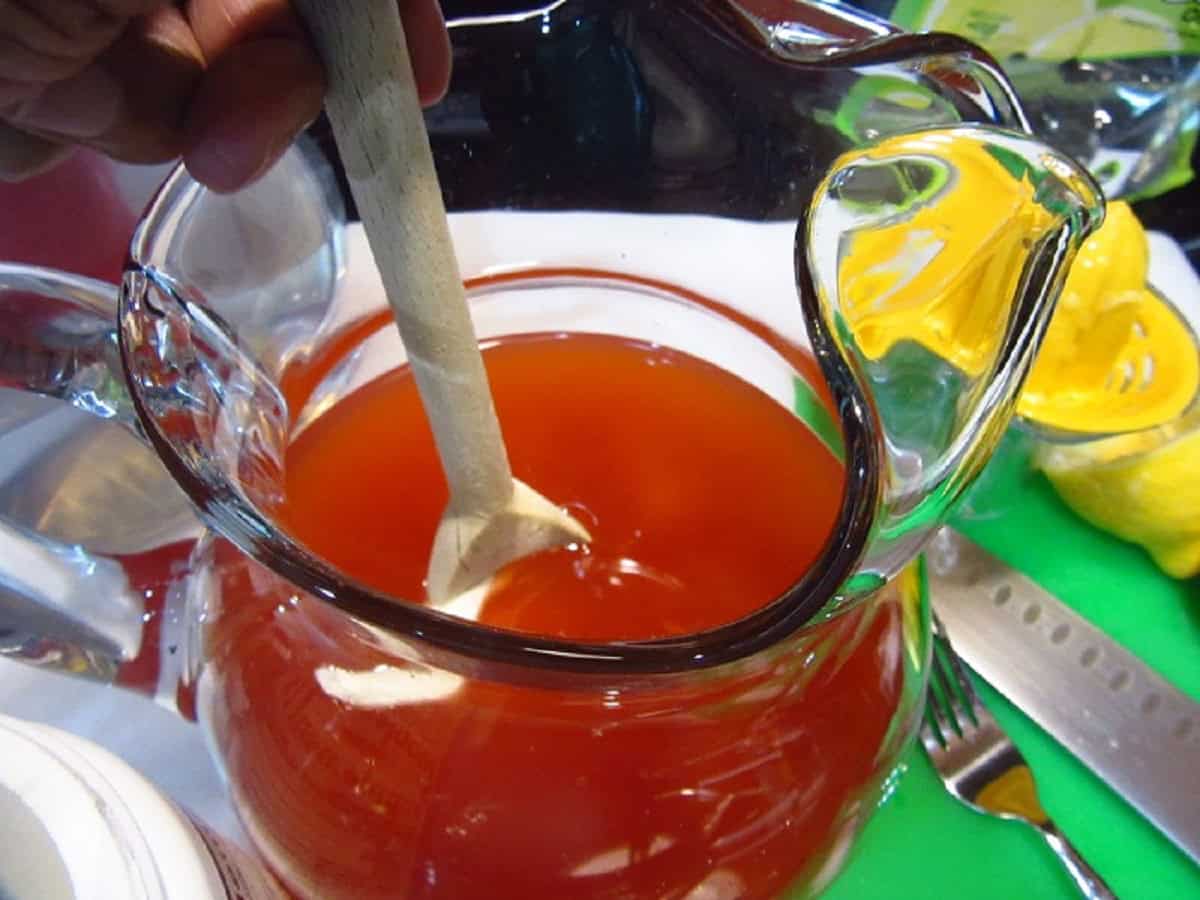 A glass pitcher with pink lemonade and a wooden spoon.